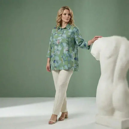 Жена облечена с зелена туника в размер 5XL с флорален десен комбинирана със светъл панталон в студио със зелен фон и декоративна форма