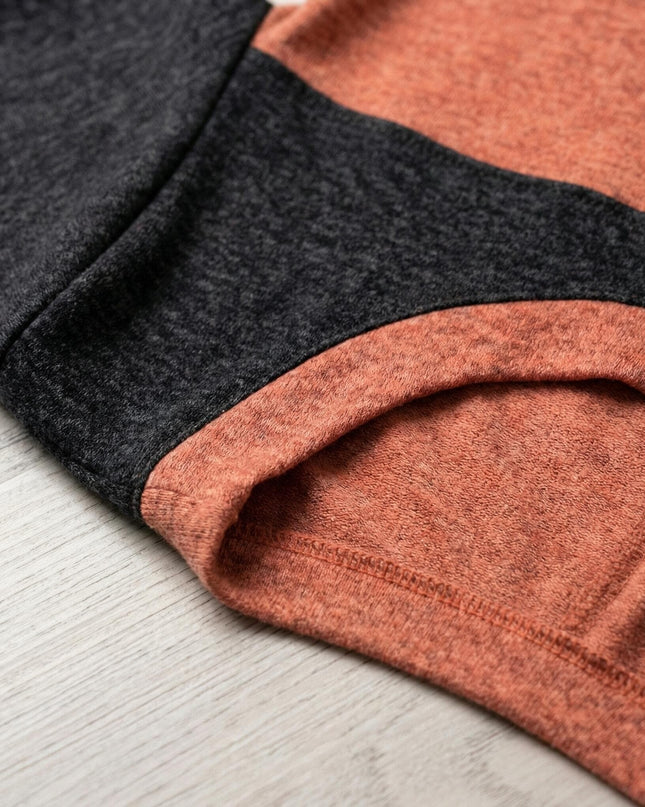 Детайл отблизо на меката материя и шевовете на асиметрична зимна туника в корал и графит, показващ текстурата на плата.