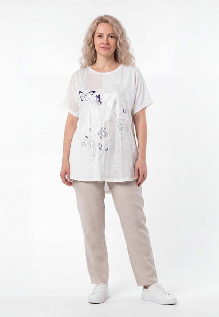 Бяла лятна памучна туника с флорална апликация и къс ръкав, представена от модел в цял ръст, съчетана със светъл панталон.