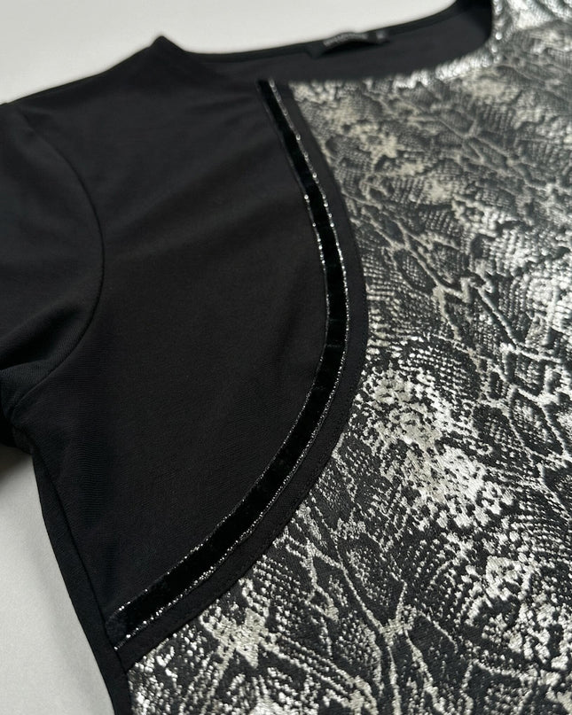 Детайл отблизо на черна макси туника, акцентиращ върху съчетанието на изчистена черна материя, сребрист змийски принт и блестящ кант.