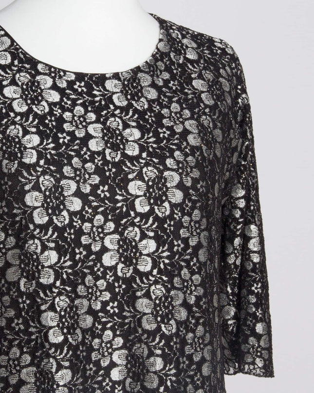 Детайлен кадър на черна официална рокля с флорална дантела, фокусиран върху облото деколте и красивите сиви цветя върху черната материя.