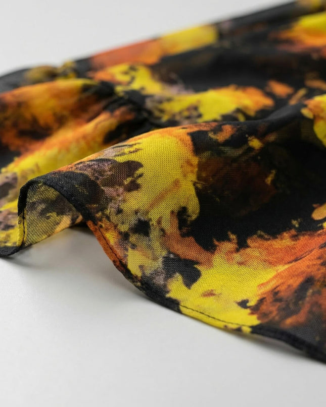 Детайл отблизо на ефирната материя на черна официална шифонена рокля с абстрактен принт в топли жълти и оранжеви нюанси.