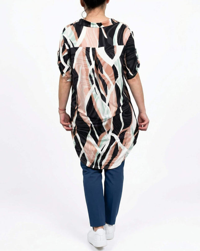 Дълга лятна макси туника с шарен принт и асиметрична кройка. Изглед отзад в цял ръст на бял фон, съчетана със син панталон.