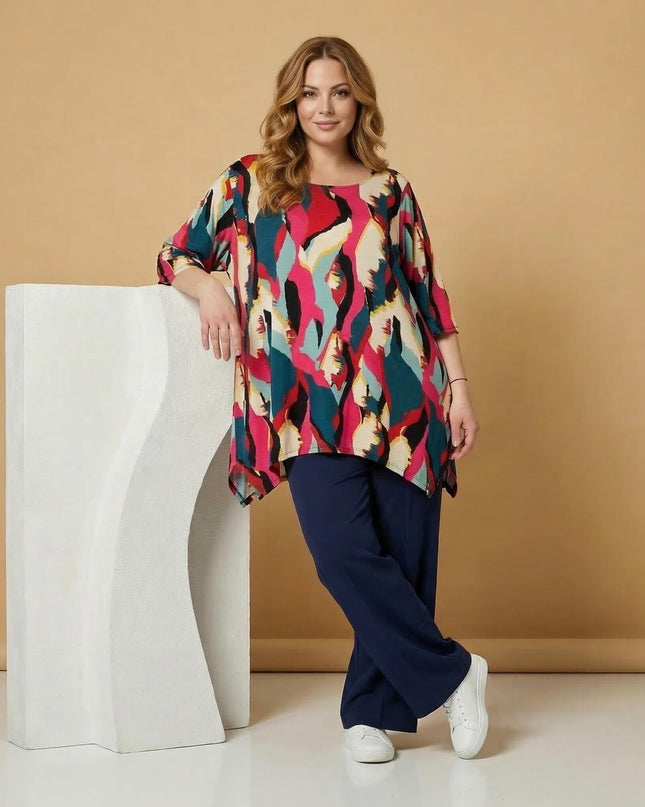 Дълга лятна макси туника в шарен абстрактен принт, представена в цял ръст върху модел, облегнат на бял декор.