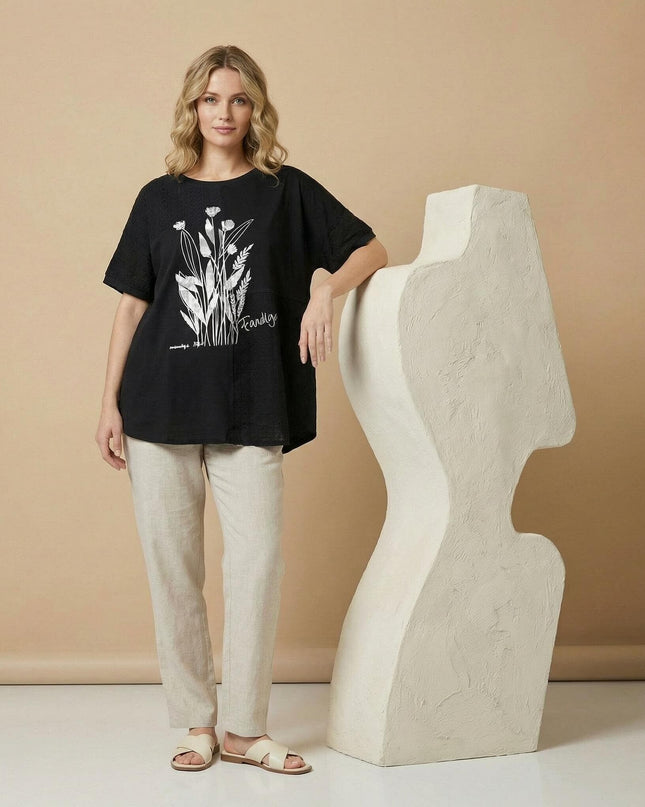 Дамска лятна макси туника в черен цвят с ефектна флорална апликация, представена в цял ръст, съчетана със светъл панталон.