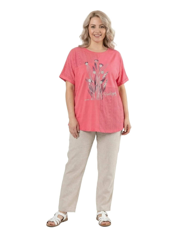 Лятна дамска туника големи размери в коралов цвят с флорален принт, заснета в цял ръст на бял фон, облечена от модел със светъл панталон.