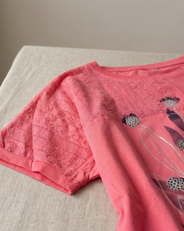 Детайл отблизо на коралова дамска лятна туника големи размери, показващ ефирния дантелен ръкав и флоралната апликация със сребристи акценти.