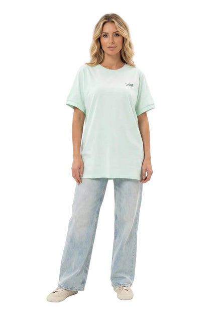 Дамска памучна макси тениска в цвят резеда с малка щампа. Моделът позира в цял ръст, облечен в свободната туника, съчетана със светли дънки.
