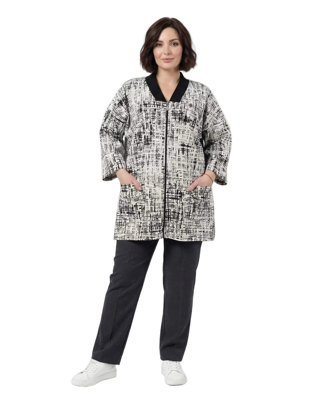 Дамски бежов макси жакет с абстрактен десен и предно закопчаване с цип. Кадър в цял ръст, показващ черната рипсена яка, 7/8 ръкави и ръце в джобовете.