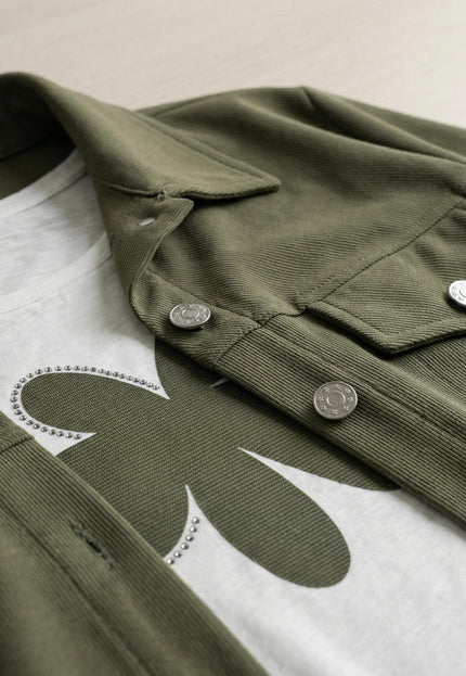 Детайл отблизо на дамски комплект в цвят каки, показващ текстурата на сакото с джоб и метални копчета, както и част от принта на бялата тениска.