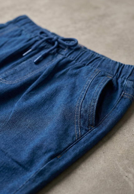 Детайл отблизо на дамски памучни дънки в син цвят, показващ удобната ластична талия с връзки, контрастни шевове и преден джоб.
