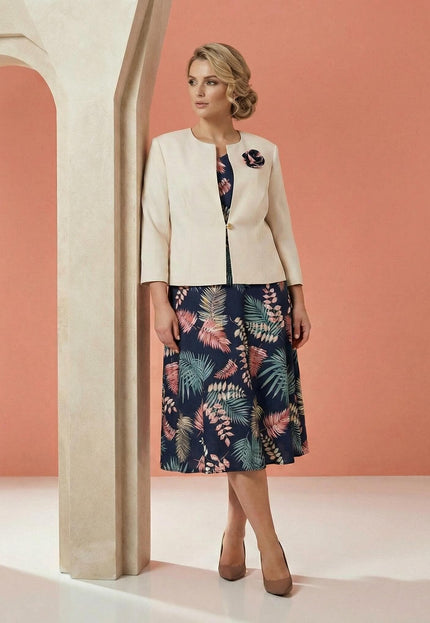 Елегантен дамски костюм големи размери, съчетаващ тъмносиня рокля на цветя и бежово сако с брошка, заснет в цял ръст.