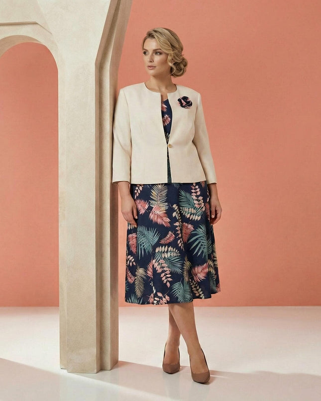 Елегантен дамски костюм големи размери, съчетаващ тъмносиня рокля на цветя и бежово сако с брошка, заснет в цял ръст.