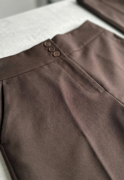 Детайл отблизо на колана с три копчета и страничния джоб на елегантен кафяв панталон с висока талия, заснет в плосък кадър.
