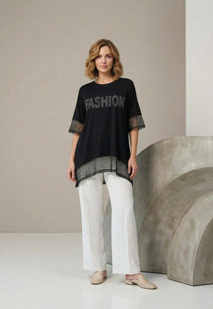 Снимка в цял ръст на елегантна черна асиметрична туника големи размери с мрежа по ръкавите и подгъва, съчетана с бели панталони.