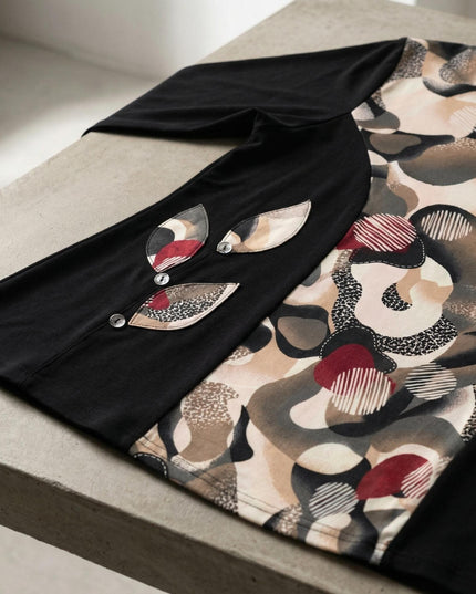 Детайлен кадър на елегантна черна туника с абстрактен цветен принт, акцентиращ върху декоративните апликации във форма на листа с копчета.