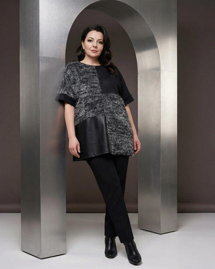 Елегантна черна туника с релефна мъхеста предна част и долен кожен панел, показана в цял ръст върху модел, позиращ до сребърна арка.