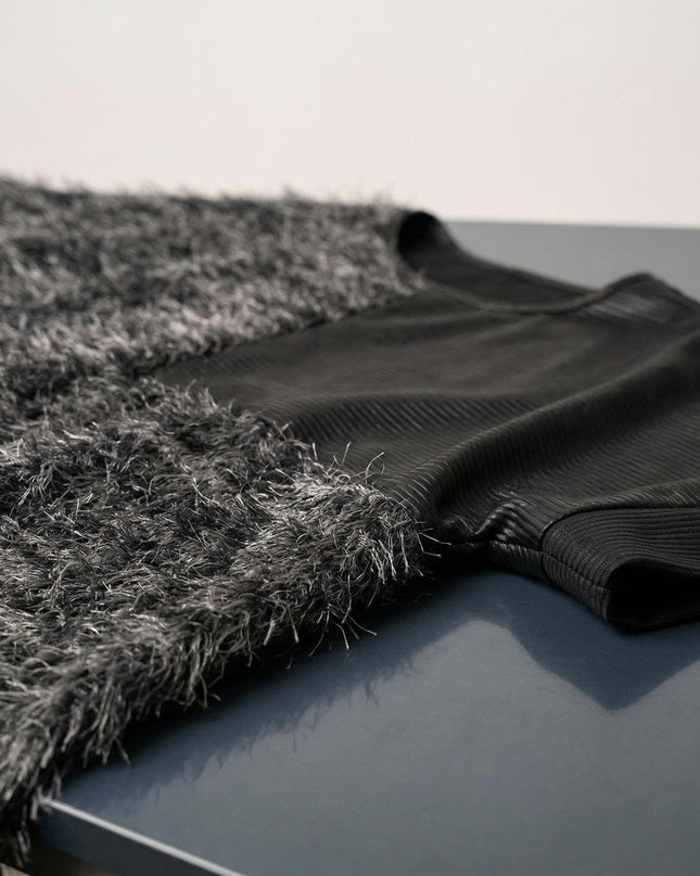 Детайлен кадър на елегантна черна туника, показващ съчетанието от релефна мъхеста материя и панел с ефект на кожа.