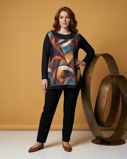 Елегантна дамска туника в черно с цветен витражен принт отпред. Моделът позира в цял ръст, демонстрирайки свободната А-образна кройка и дългите ръкави.