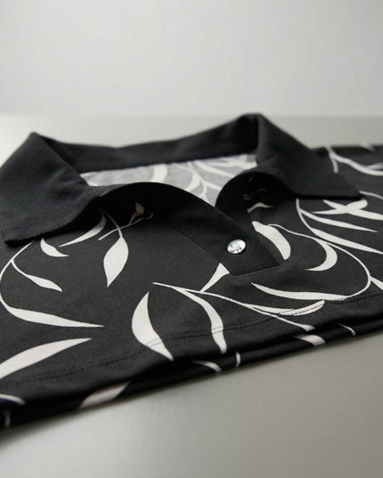 Детайлен кадър на елегантна макси туника с абстрактен принт, фокусиращ се върху черната яка и V-образното деколте с копче.