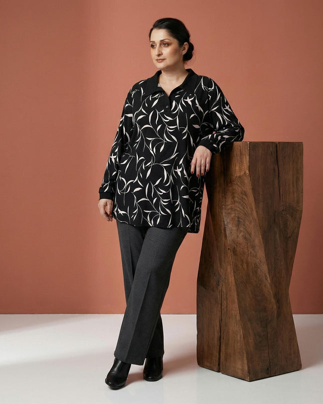 Елегантна макси туника с абстрактен принт на листа и черна яка, представена в цял ръст върху модел до дървен постамент.