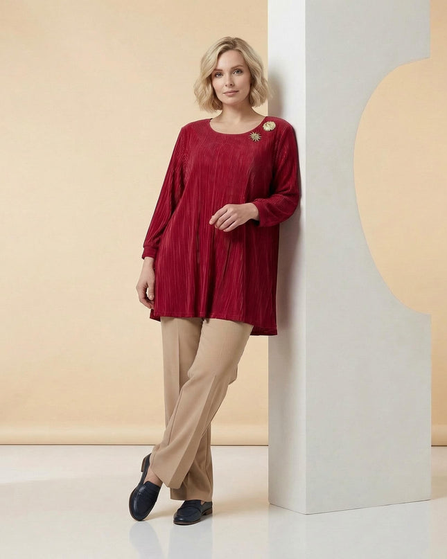 Модел в цял ръст, представящ елегантна официална макси туника в червено с фина плисирана текстура и две изящни златни брошки на деколтето.