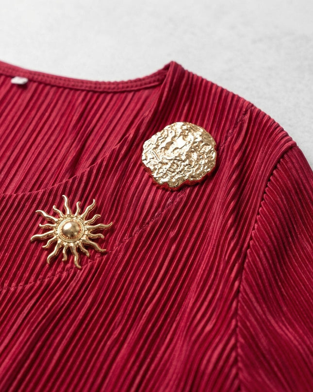 Детайл отблизо на елегантна официална макси туника в червено, показващ фината плисирана текстура и красивите златисти брошки.