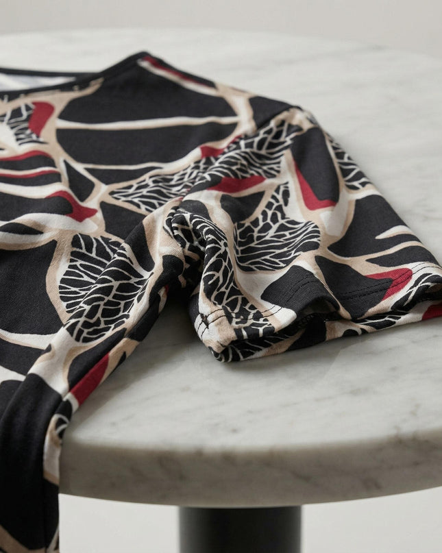 Детайл отблизо на елегантна макси туника с абстрактен вълнообразен принт в черно и червено, показващ ръкава и мекото трико върху мраморна маса.