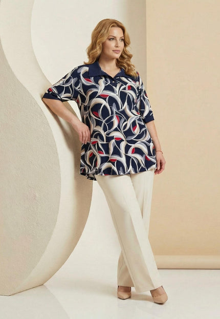 Елегантна разкроена туника големи размери в тъмносиньо с абстрактен десен, представена в цял ръст върху модел, съчетана с бежов панталон.