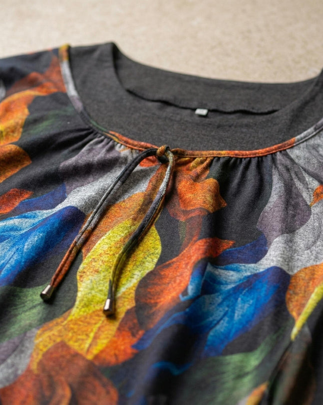 Детайл на обло деколте с връзка на елегантна туника с абстрактни цветя. Снимка отблизо, показваща материята и пъстрия десен върху черен фон.