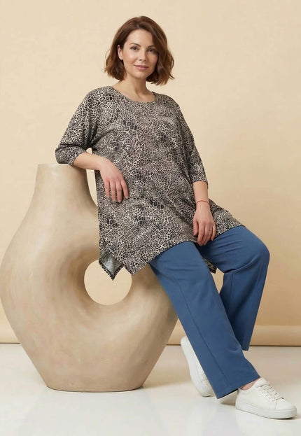 Ежедневна макси туника с леопардов десен и 3/4 ръкави. Кадър в цял ръст на модел, облегнат на декоративна фигура, в съчетание със син панталон.