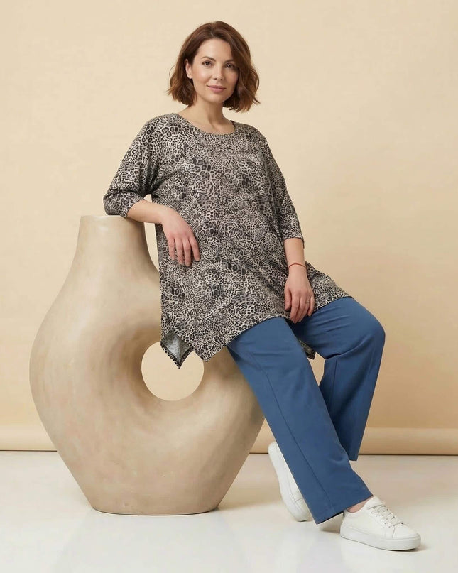 Ежедневна макси туника с леопардов десен и 3/4 ръкави. Кадър в цял ръст на модел, облегнат на декоративна фигура, в съчетание със син панталон.