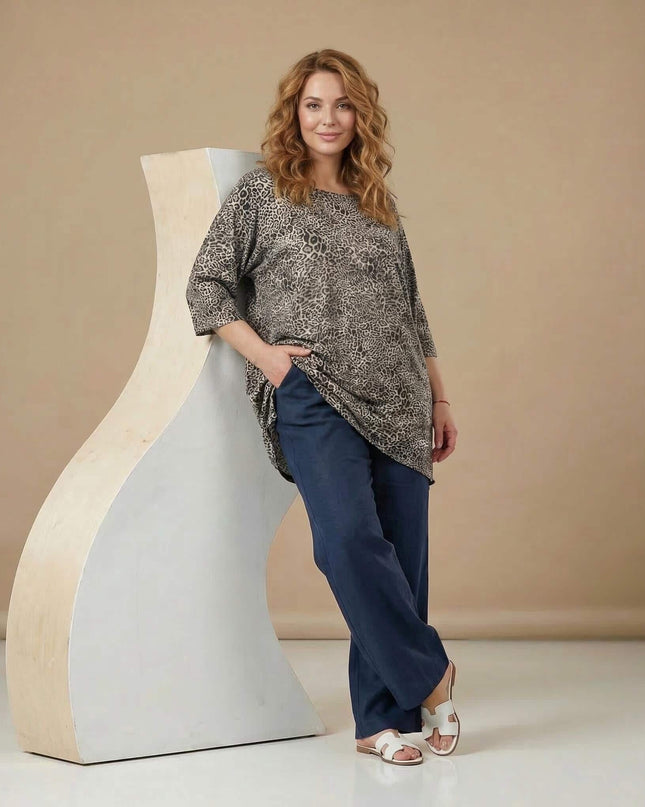 Цял ръст на жена, облечена в ежедневна макси туника с леопардов десен. Свободната кройка с 3/4 ръкави е съчетана с тъмносин панталон и сандали.