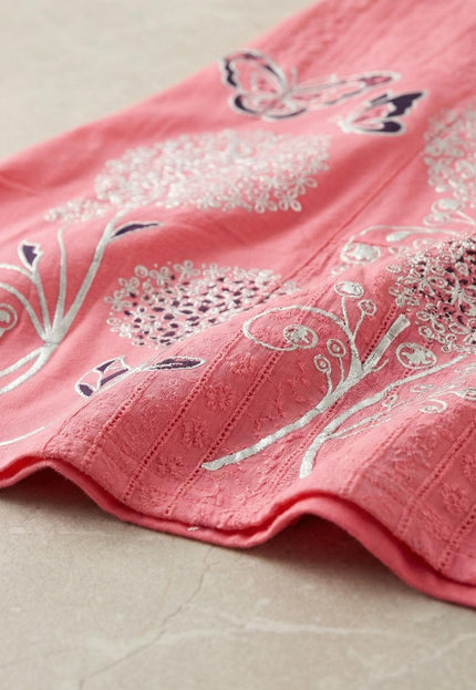 Детайл отблизо на лятна памучна туника в цвят корал. Вижда се текстурата на плата и красивата сребриста апликация на цветя и пеперуди.