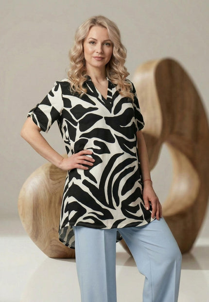 Макси лятна туника с асиметрична кройка и черно-бял абстрактен принт. Заснета отпред в 3/4 кадър върху модел със светлосини панталони.