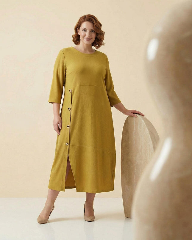 Дамска макси официална рокля в цвят горчица с асиметрични декоративни копчета. Кадър в цял ръст, показващ елегантната кройка с фина странична цепка.
