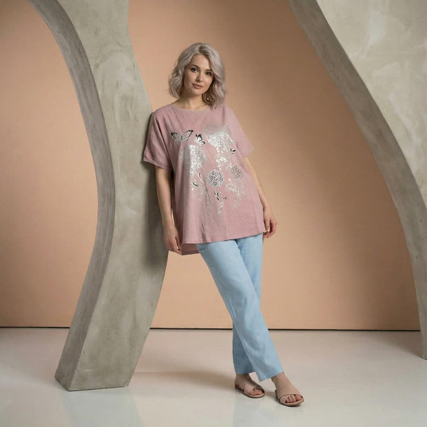 Дама с розова туника с декоративен принт и светлосин панталон в студийна обстановка с неутрален фон