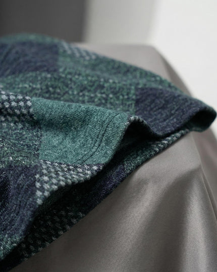 Детайл отблизо на материята на масленозелена разкроена рокля, показващ текстурата на мекото трико и геометричния пачуърк принт в тъмни нюанси.