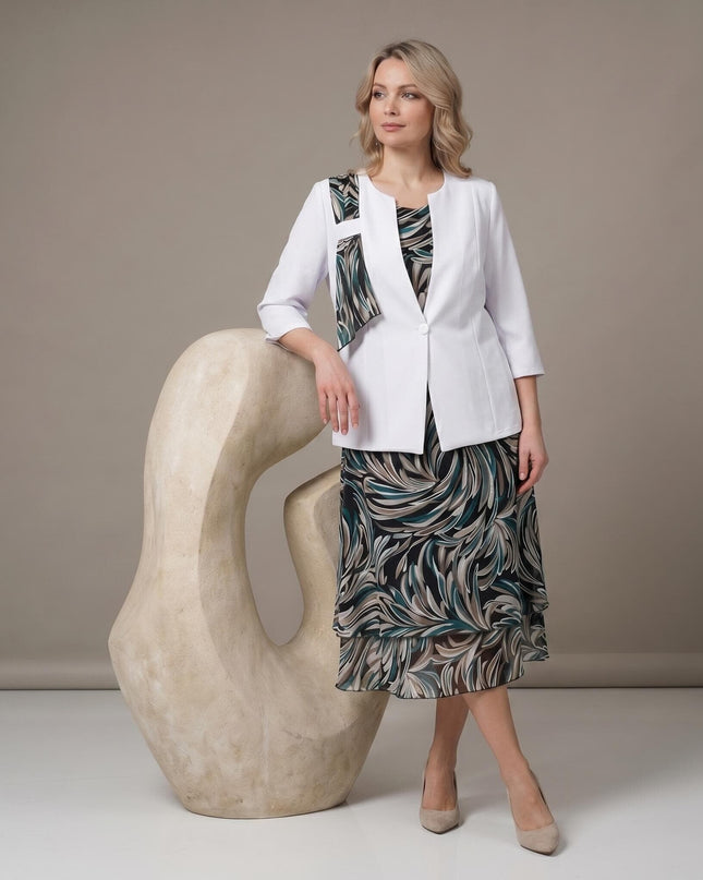Официален дамски костюм от две части с шарена шифонена рокля и бяло сако, големи размери. Моделът е сниман в цял ръст до изящна декоративна скулптура.