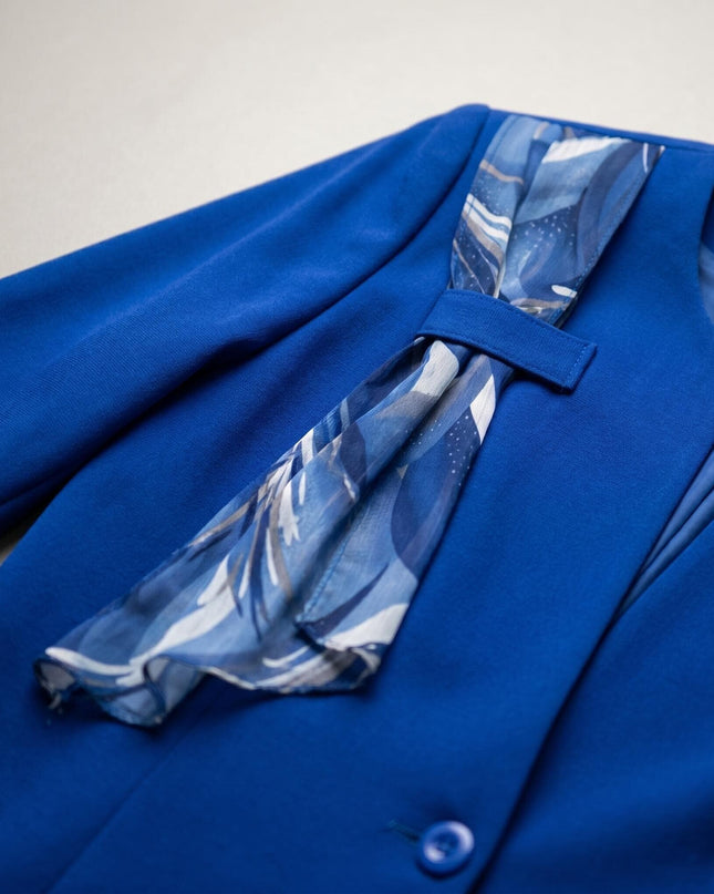 Детайл отблизо на официален дамски костюм в кралскосин цвят. Показан е реверът на сакото с декоративен шифонен акцент с абстрактен принт и едно копче.