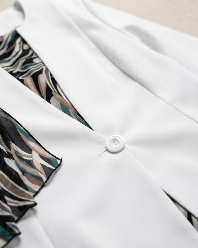 Детайл отблизо на бяло сако с едно копче, разкриващо шарена шифонена рокля от елегантен дамски костюм.
