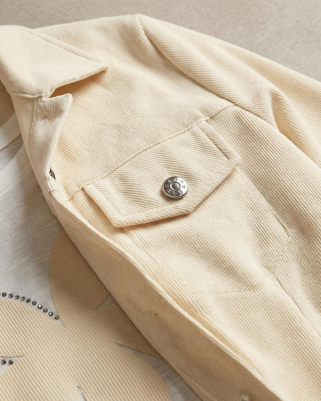 Детайл отблизо на сако в цвят екрю от макси сет, показващ релефната материя, джоб с метално копче и част от блузата с камъни.