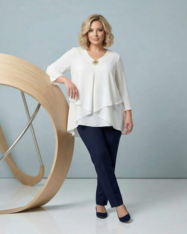 Модел в цял ръст, облечен с официална бяла макси туника с асиметрична кройка на пластове, 7/8 ръкави и златна брошка.