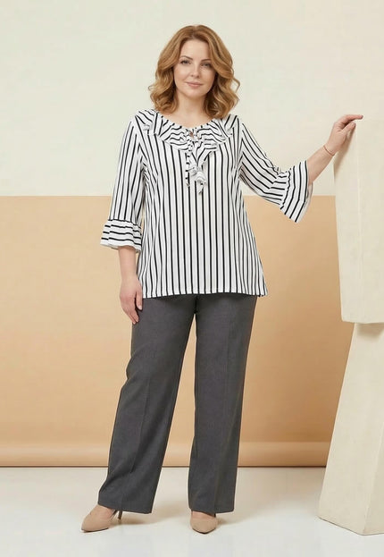 Кадър в цял ръст на дама, облечена в официална бяла туника на тъмносиньо райе с разкроени ръкави и ефектно деколте, съчетана със сив панталон.