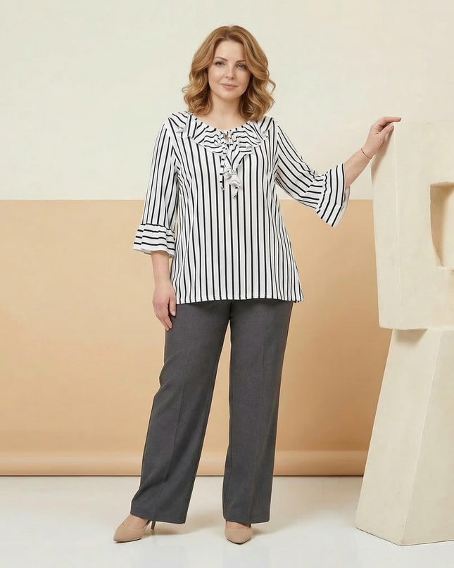 Кадър в цял ръст на дама, облечена в официална бяла туника на тъмносиньо райе с разкроени ръкави и ефектно деколте, съчетана със сив панталон.