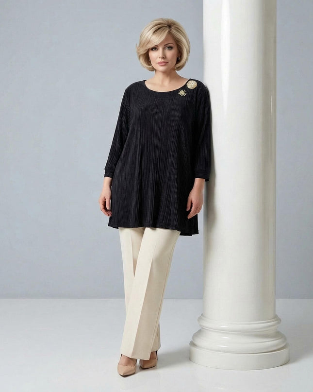 Официална черна макси туника от солей с брошка, 3/4 ръкави и деколте тип лодка. Цял ръст на жена до бяла колона, носеща светъл панталон.