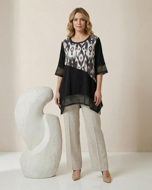 Официална черна макси туника с диагонален принт и асиметрична кройка с мрежа, показана в цял ръст върху модел, съчетана със светъл панталон.