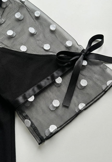 Детайл отблизо на ръкава на черна туника големи размери, декориран с прозрачен тюл на бели точки и елегантна черна панделка.