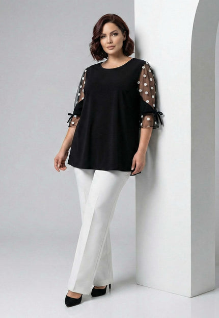 Елегантна черна туника големи размери с тюлени ръкави на бели точки и панделки. Снимка в цял ръст на модел, показваща свободната кройка и дължина.