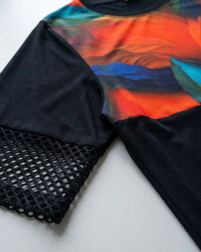 Детайл отблизо на официална черна туника, показващ ефектен мрежест ръкав и цветна абстрактна платка, заснет като плосък кадър.